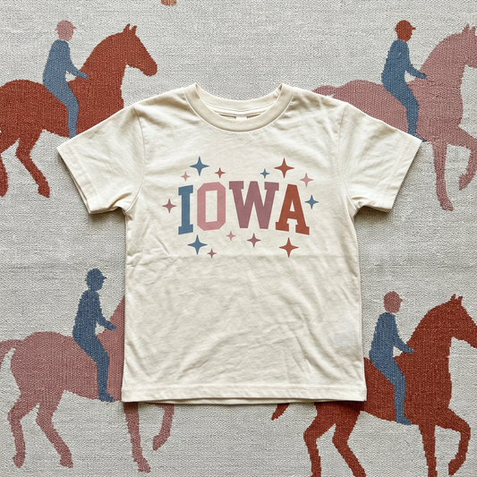 White t-shirt with 'IOWA' printed on it against a background with horse and rider illustrations.