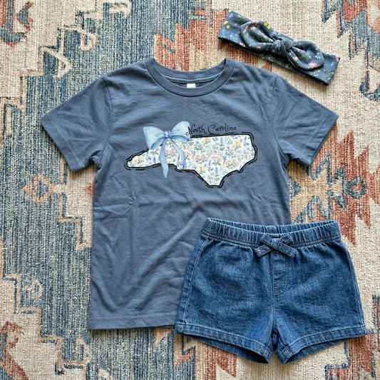 Blue t-shirt with North Carolina design, denim shorts, and headband on a patterned rug.