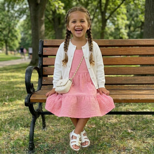 Young girl in a pink dress sitting on a wooden bench in a park.