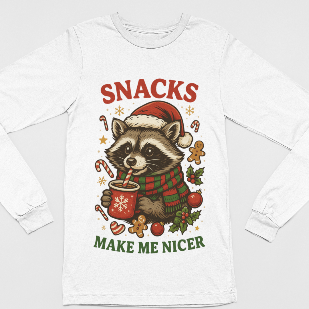 White long-sleeve kids Christmas shirt featuring a raccoon in a Santa hat and plaid scarf holding a red cocoa mug, surrounded by candy canes, gingerbread cookies, holly, and the festive phrase “Snacks Make Me Nicer.”