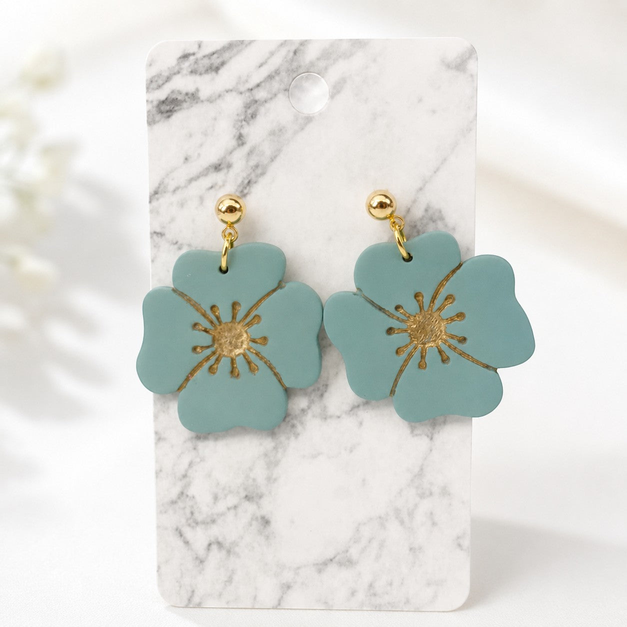 Tea-Shirt Shoppe Palm & Petal Collection earrings featuring matte teal flower charms with gold center details.