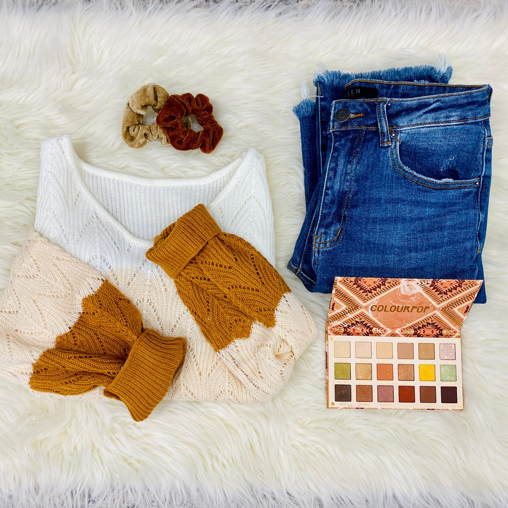 flatlay of sweater with jeans, eyeshadow, and scrunchie
