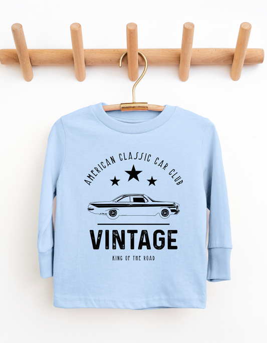 Light blue long-sleeve shirt with vintage car design on a wooden hanger against a white background