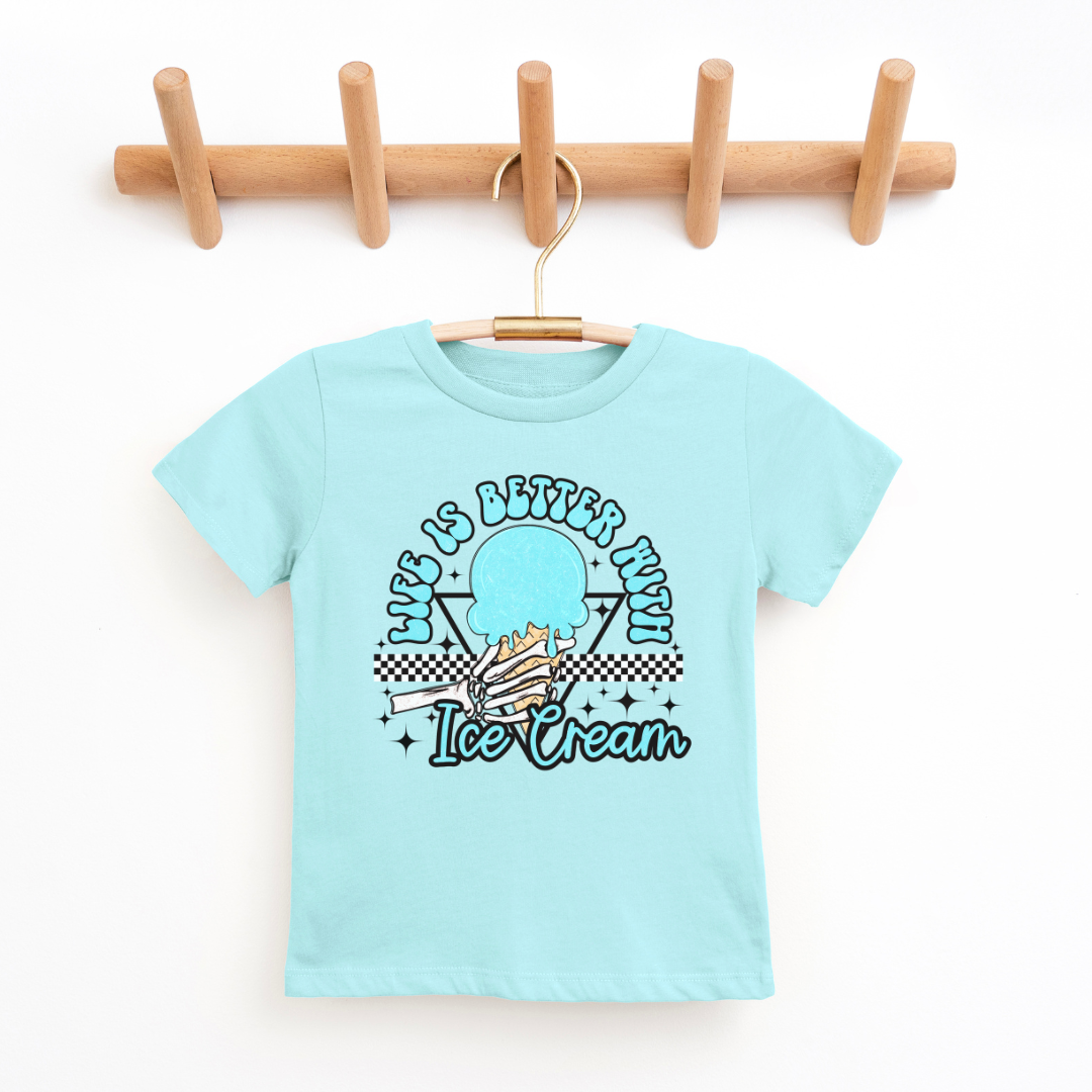 A blue kids' graphic t-shirt displayed on a wooden hanger against a clean, white background. The shirt features a colorful design in the center with the phrase "Life is Better with Ice Cream" in playful lettering, encircling a stylized image of an ice cream cone with a checkered motif at the bottom. The t-shirt has a classic crew neckline and short sleeves, suggesting a comfortable and casual style. The hanger is mounted on a wooden rack with four pegs, providing a natural and simple presentation.