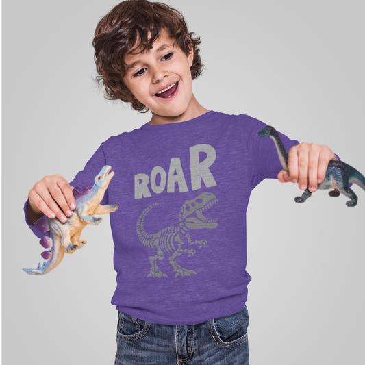 Child wearing a purple shirt with dinosaur design and 'ROAR' text, holding toy dinosaurs against a gray background