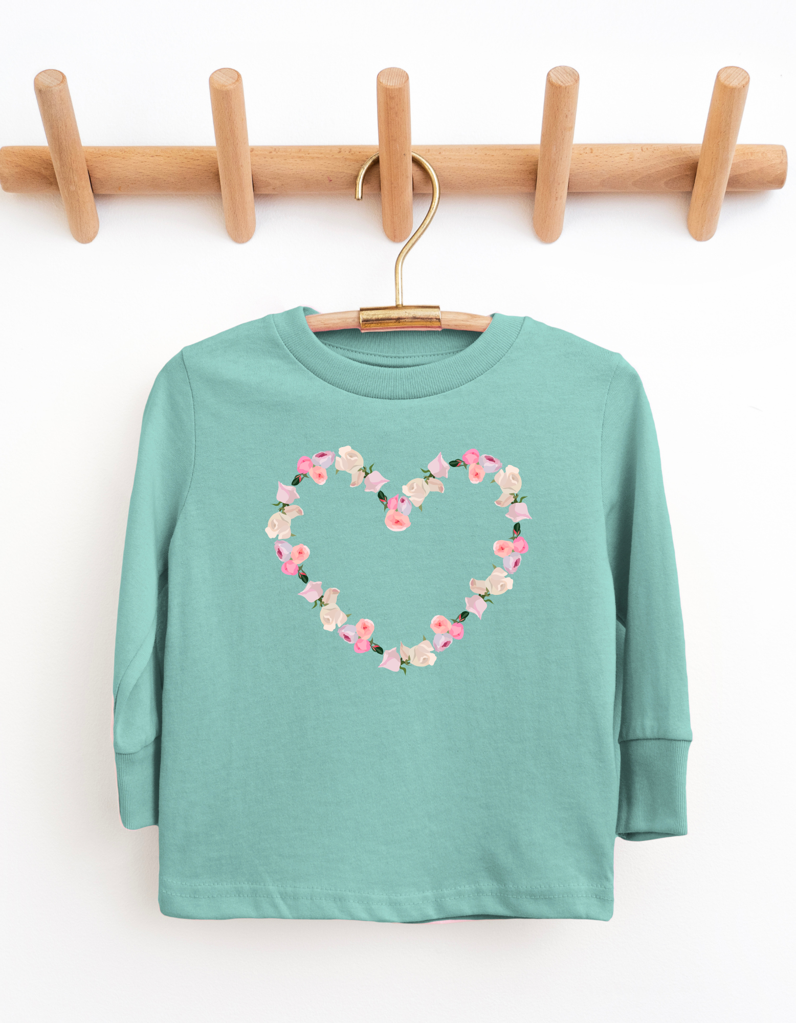 Teal long-sleeve shirt with a floral heart design on a wooden hanger against a white background