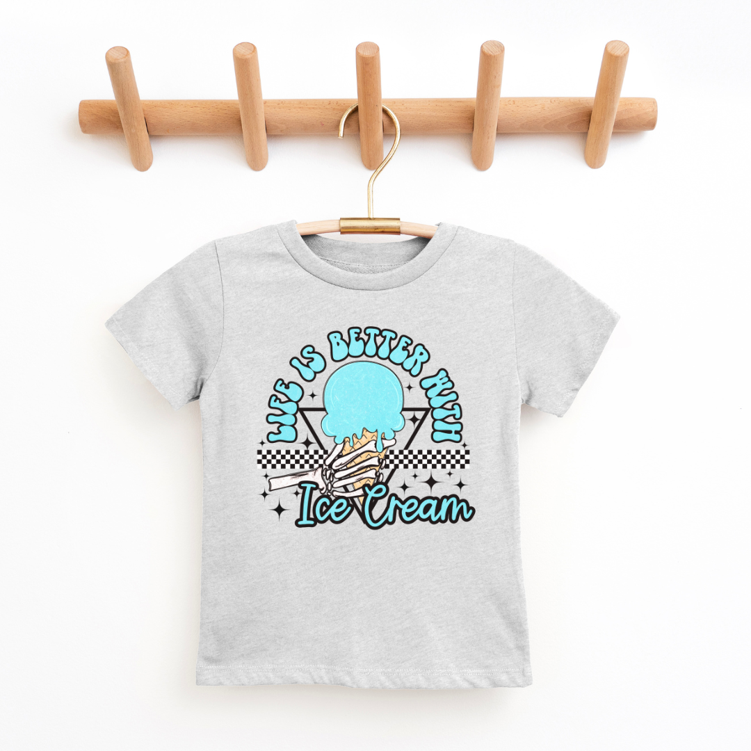 A heather-gray kids' graphic t-shirt displayed on a wooden hanger against a clean, white background. The shirt features a colorful design in the center with the phrase "Life is Better with Ice Cream" in playful lettering, encircling a stylized image of an ice cream cone with a checkered motif at the bottom. The t-shirt has a classic crew neckline and short sleeves, suggesting a comfortable and casual style. The hanger is mounted on a wooden rack with four pegs, providing a natural and simple presentation.