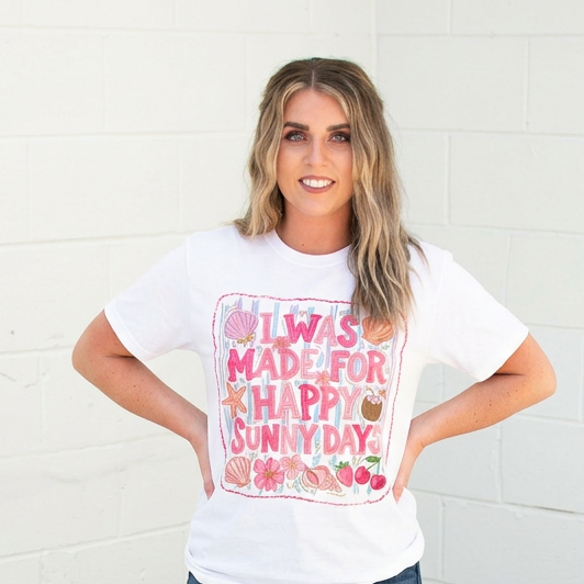Woman wearing a white t-shirt with colorful text and graphics, standing against a white brick wall.