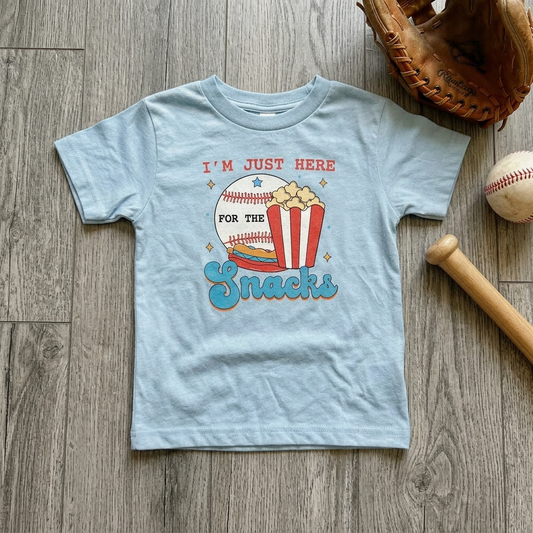 Light blue t-shirt with a graphic design of popcorn and baseball, placed on a wooden surface with a baseball and glove.