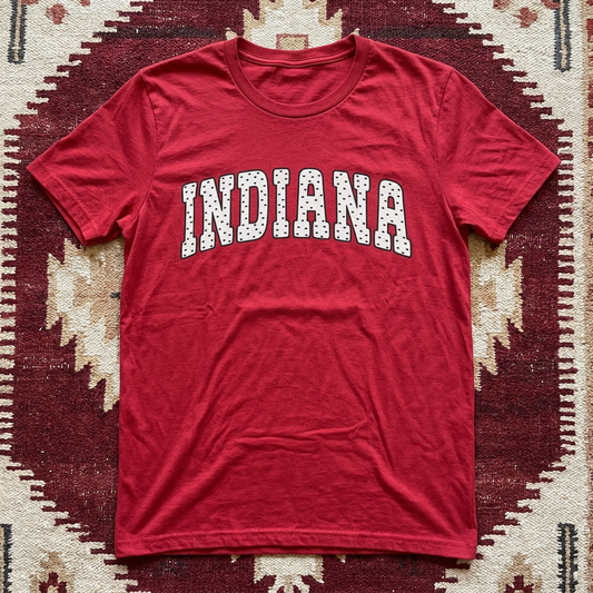 Red t-shirt with 'INDIANA' printed on it, laid flat on a patterned surface.