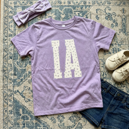 Purple t-shirt with 'IA' design, headband, and shoes on a patterned rug