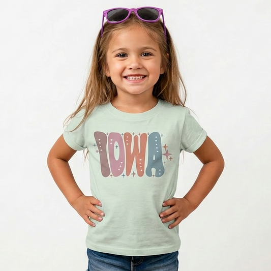 Young girl wearing a light green t-shirt with 'IOWA' printed on it, standing against a white background.