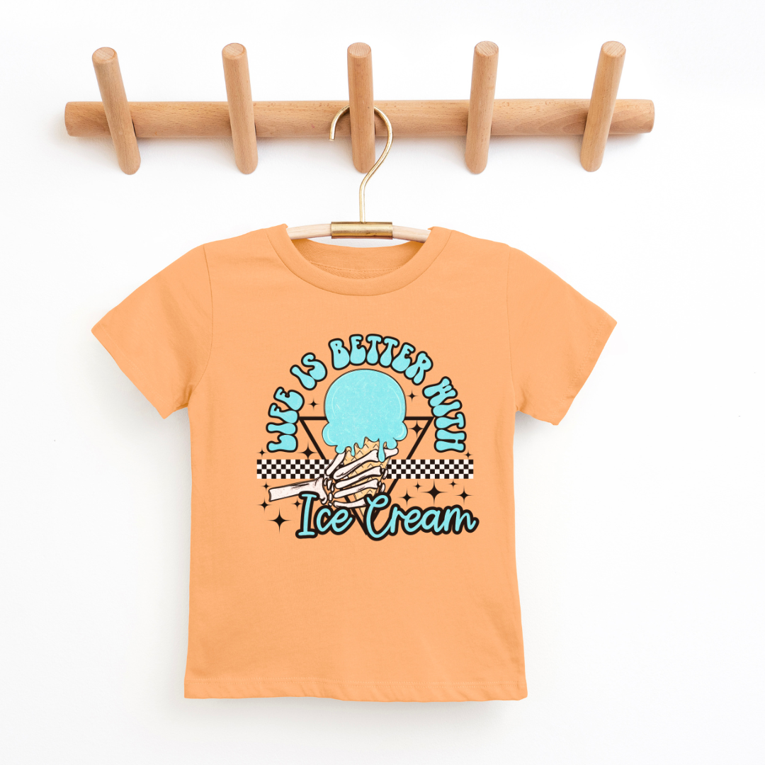 A papaya peach kids' graphic t-shirt displayed on a wooden hanger against a clean, white background. The shirt features a colorful design in the center with the phrase "Life is Better with Ice Cream" in playful lettering, encircling a stylized image of an ice cream cone with a checkered motif at the bottom. The t-shirt has a classic crew neckline and short sleeves, suggesting a comfortable and casual style. The hanger is mounted on a wooden rack with four pegs, providing a natural and simple presentation.