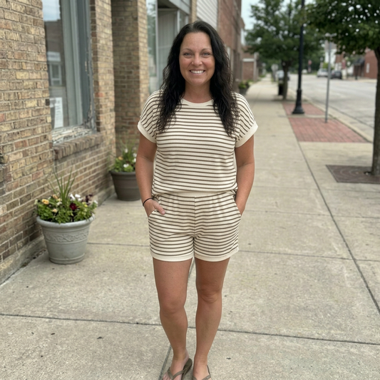 Woman in a striped romper standing on a sidewalk next to a brick building.