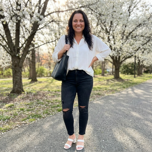Woman in white blouse and black jeans standing on a path with blooming trees in the background