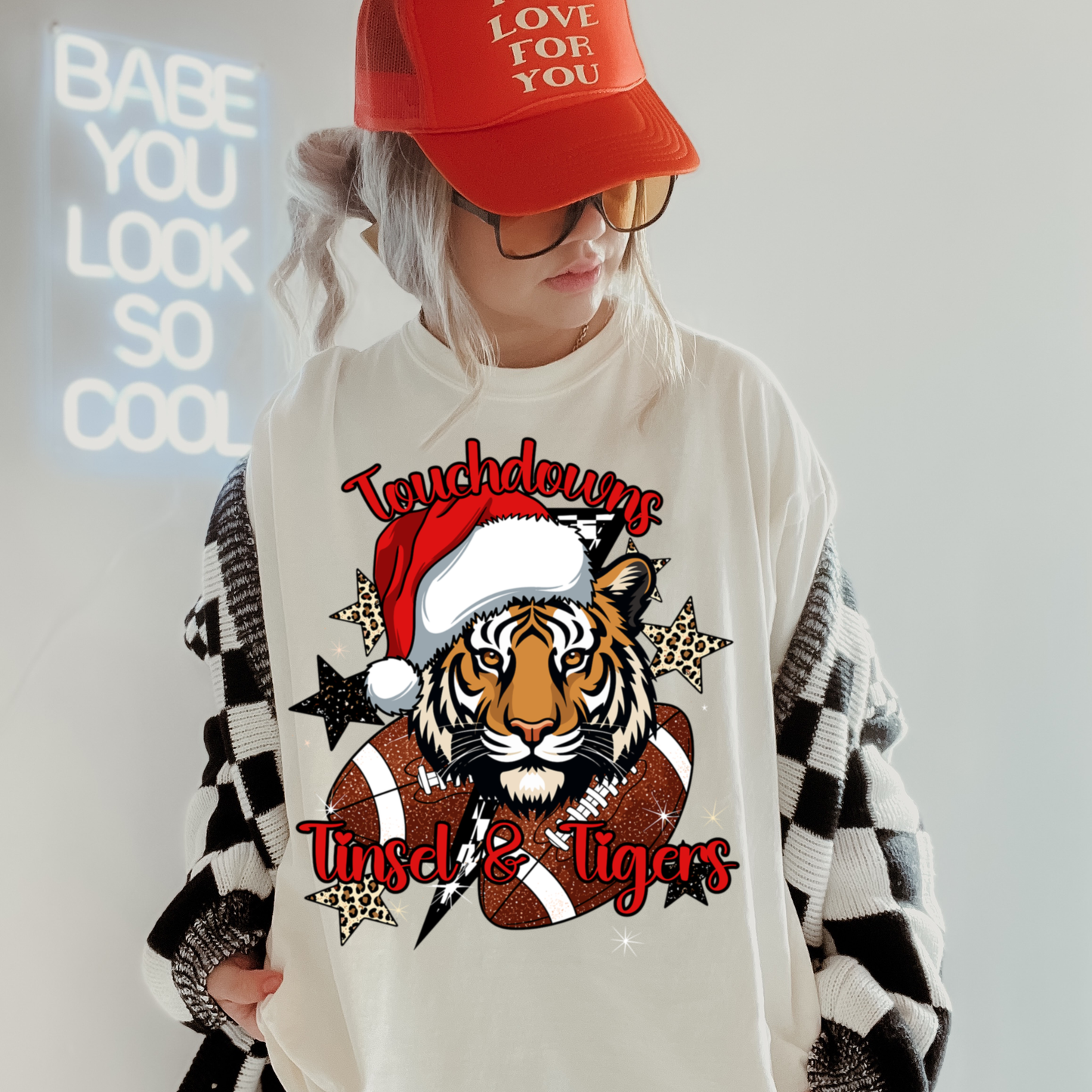 Person wearing a white sweatshirt with a tiger graphic and text, red cap, and plaid jacket.