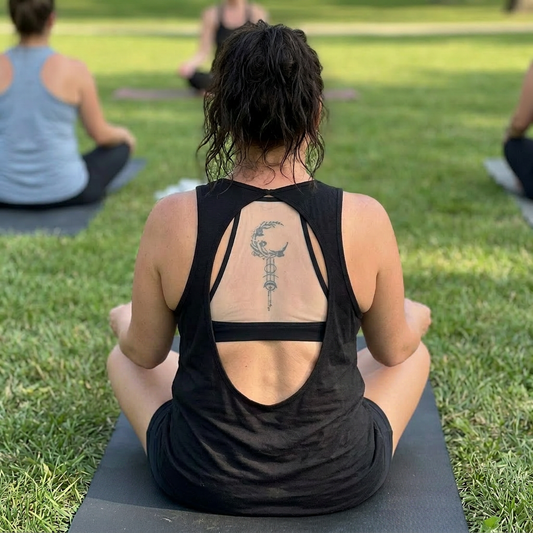 Person sitting on a yoga mat outdoors with a tattoo visible on their back