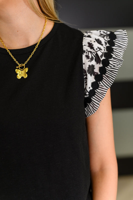 Tea-Shirt Shoppe black ribbed knit top featuring woven flutter sleeves with floral and striped patterns.