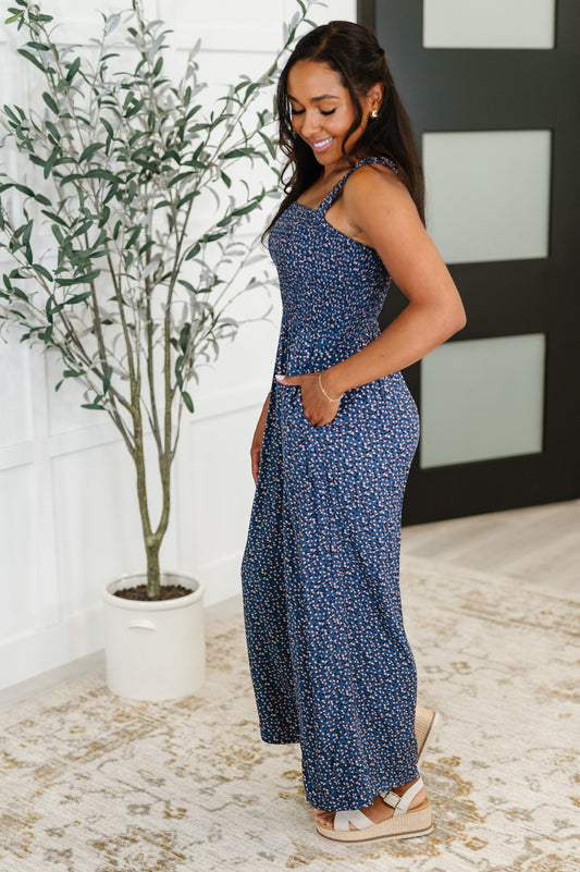 Tea-Shirt Shoppe blue floral poplin jumpsuit with a smocked bodice, square neckline, and side pockets on a model.