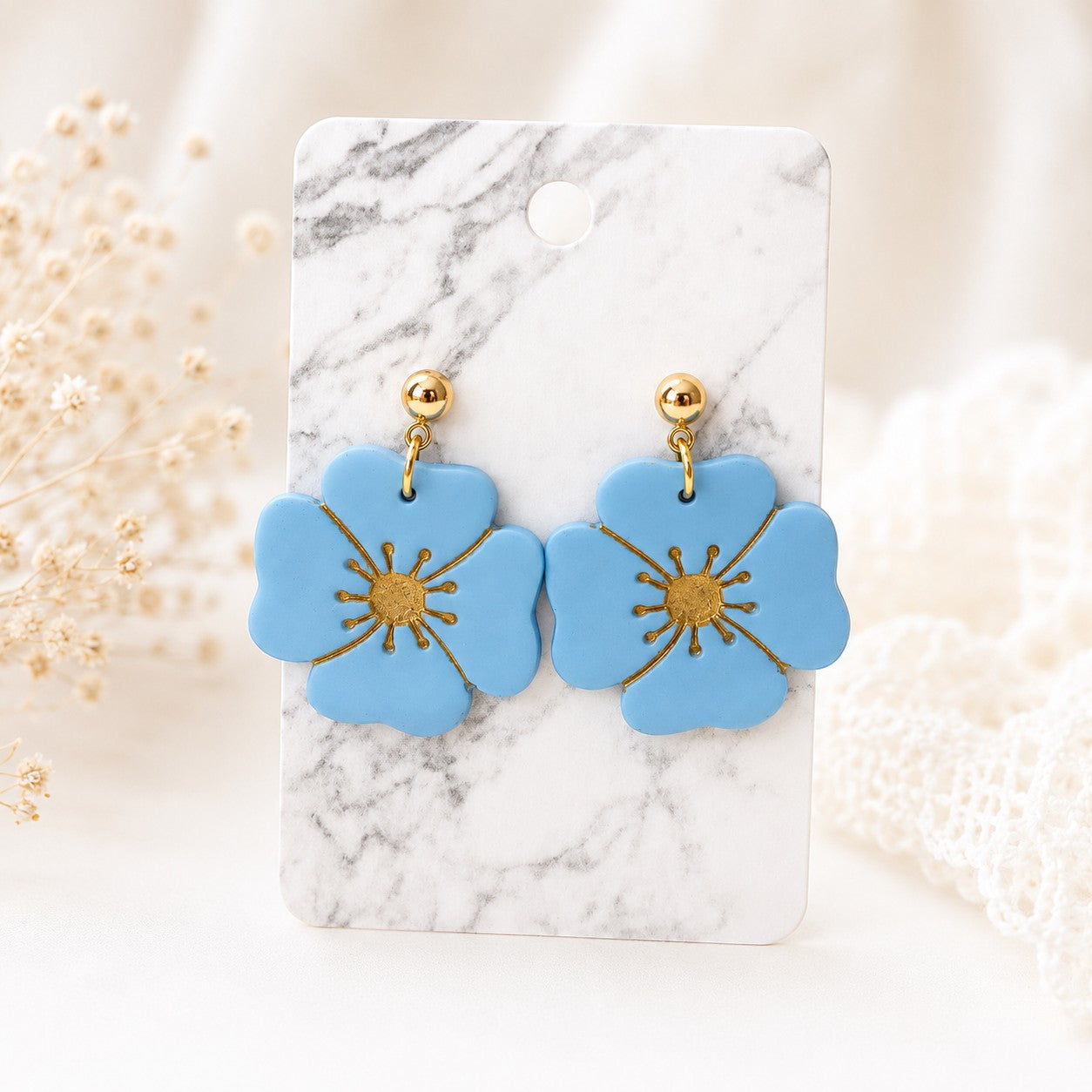 Tea-Shirt Shoppe Palm & Petal Collection blue flower-shaped polymer clay earrings with gold centers on marble card