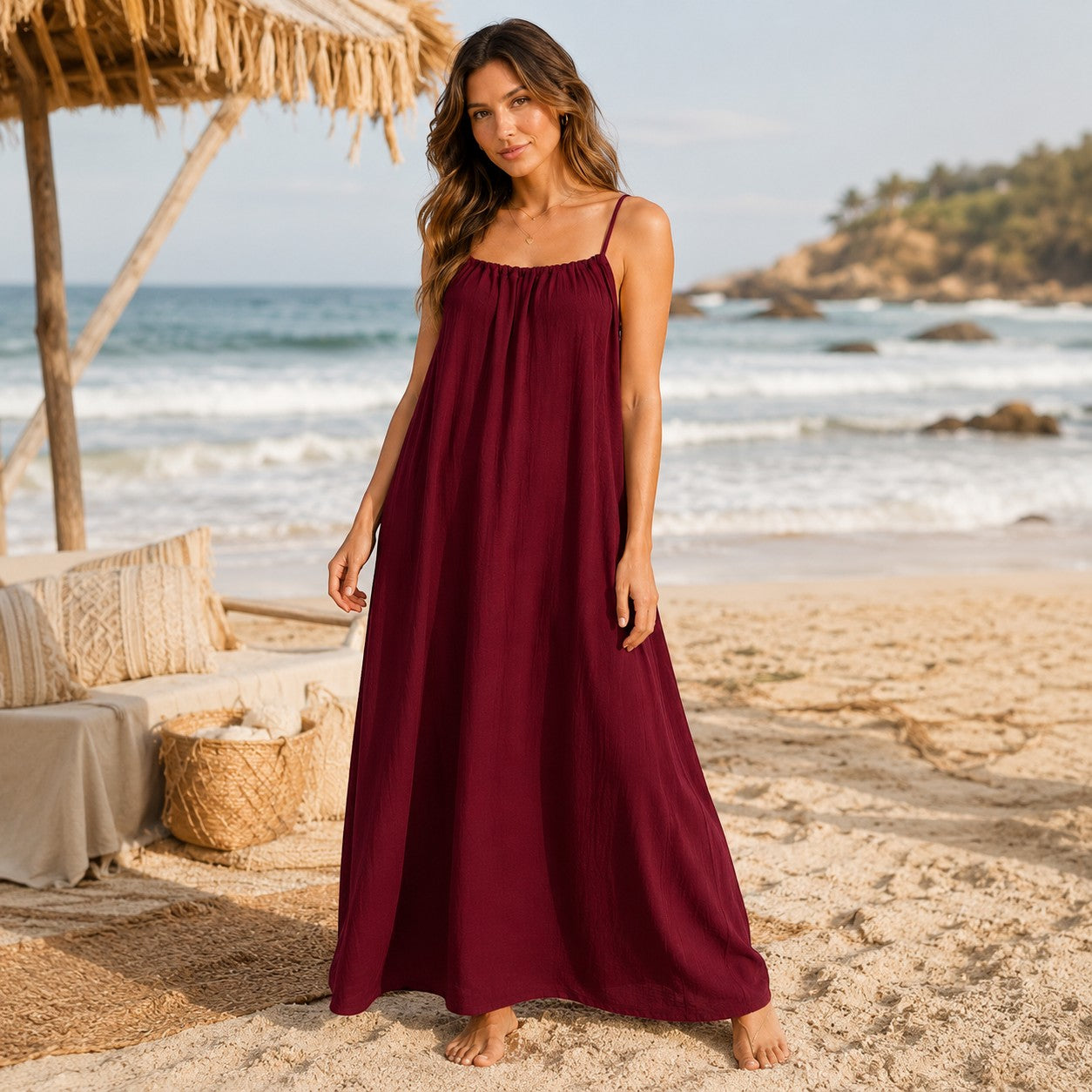 Woman wearing a burgundy Tea-Shirt Shoppe spaghetti strap maxi dress on a beach with a boho aesthetic.