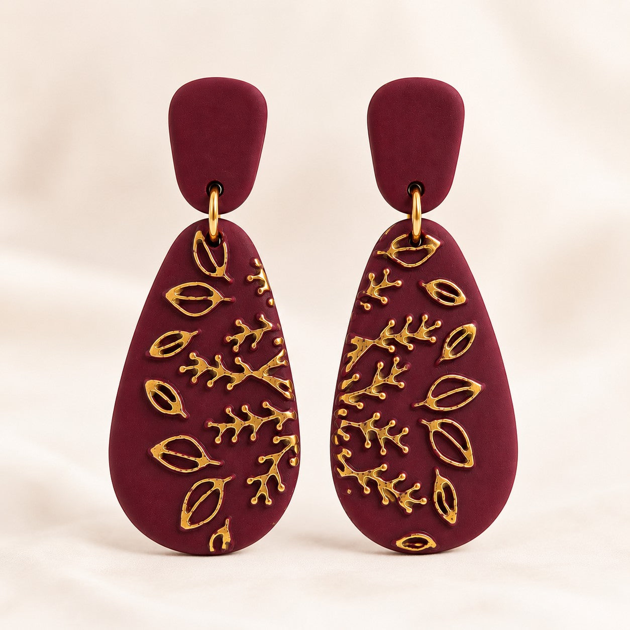 Tea-Shirt Shoppe burgundy matte teardrop dangle earrings with gold-toned botanical leaf and branch detailing.