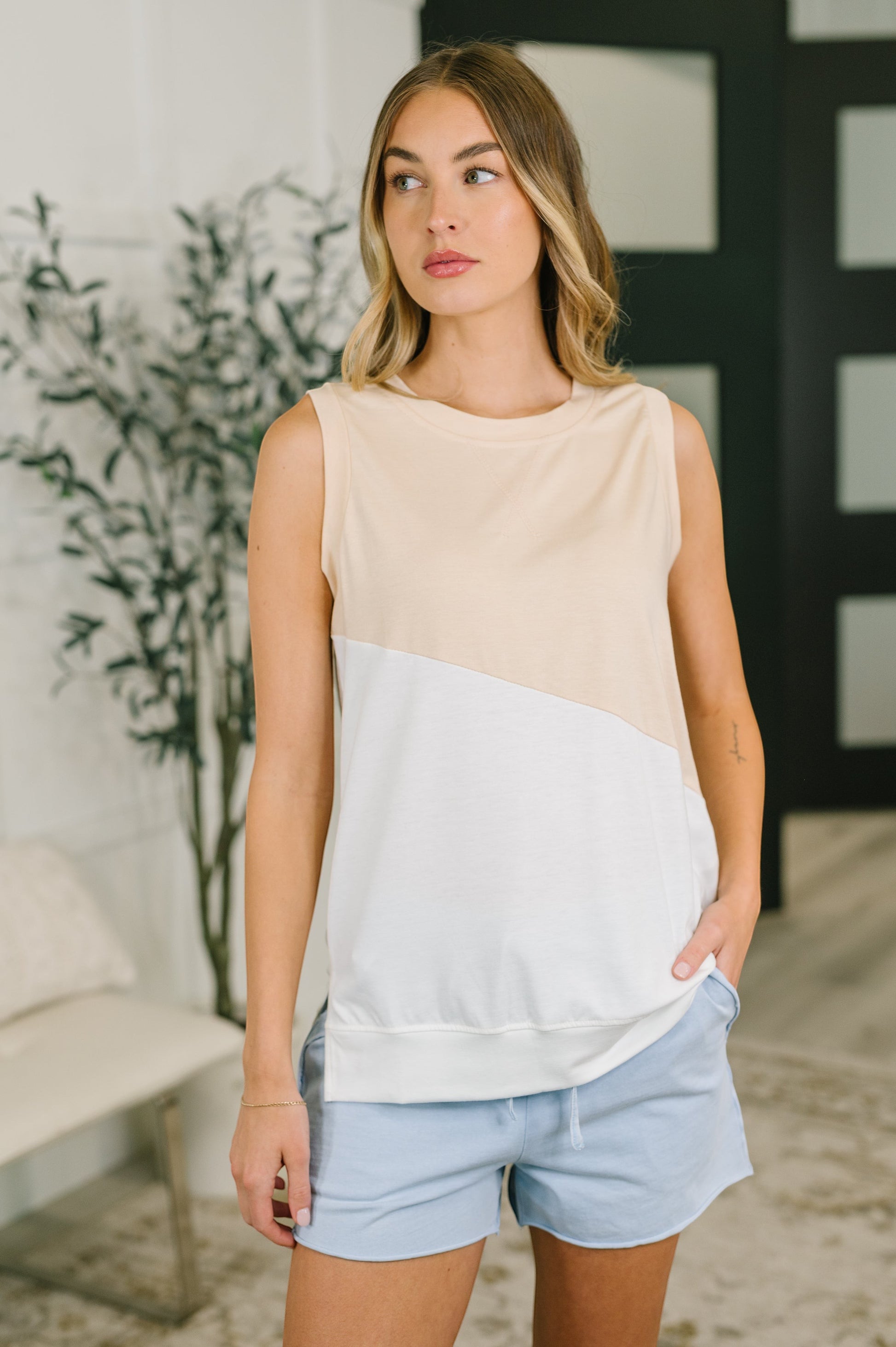 Model wearing Tea-Shirt Shoppe sleeveless jersey knit top with beige and white slanted color block detail and side slits