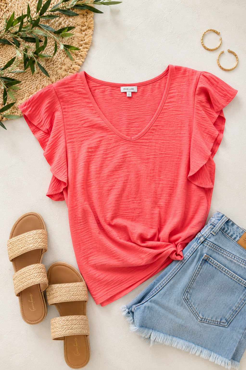 Tea-Shirt Shoppe coral crinkle woven V-neck top with flutter sleeves and a back tie, styled with denim shorts.