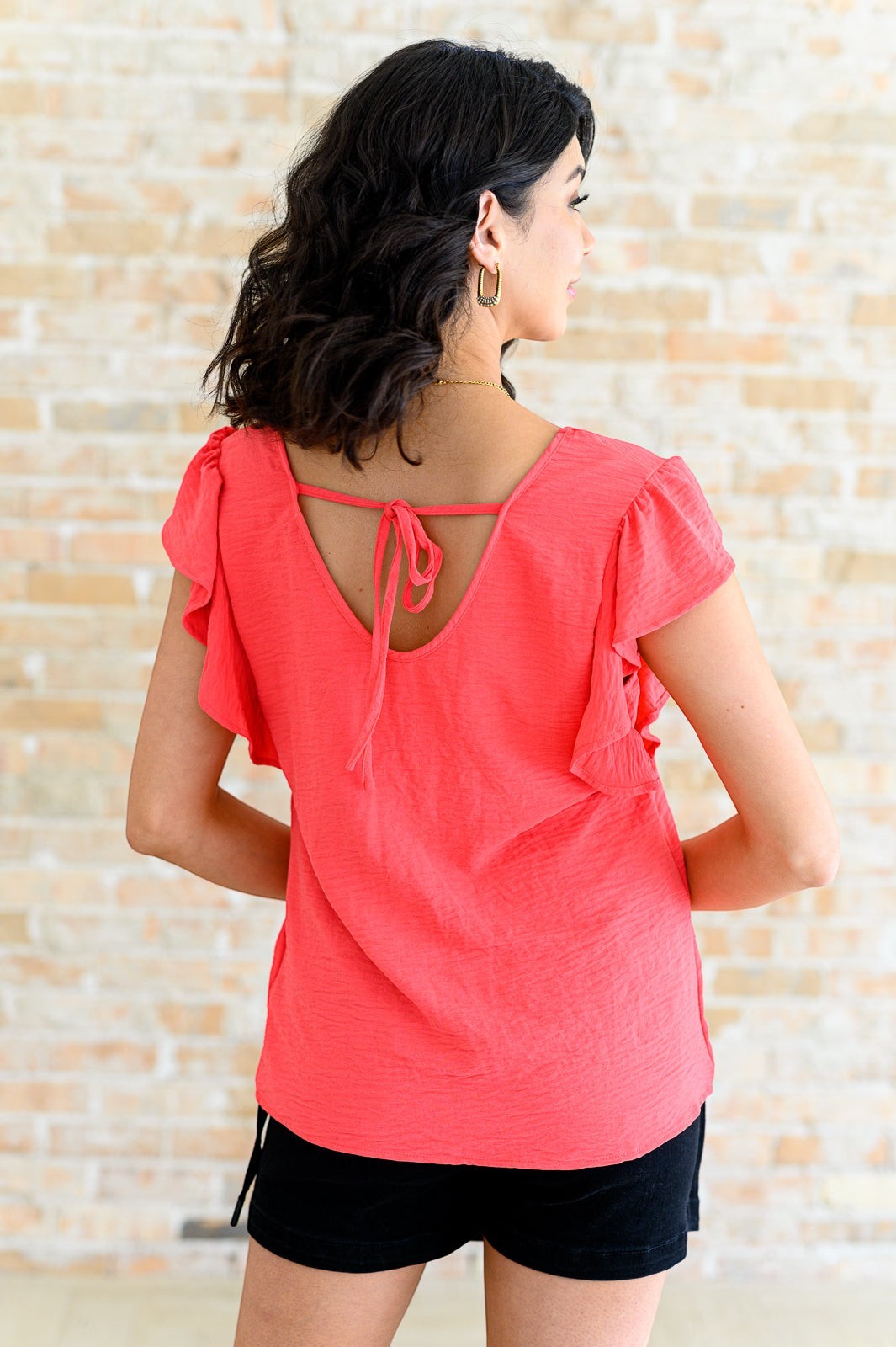 Tea-Shirt Shoppe coral crinkle woven top with flutter sleeves and a functional back tie worn by a model