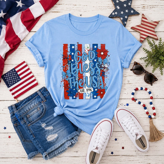 Tea-Shirt Shoppe light blue graphic tee with "God Bless the USA" text, floral accents, and red, white, and blue stripes.