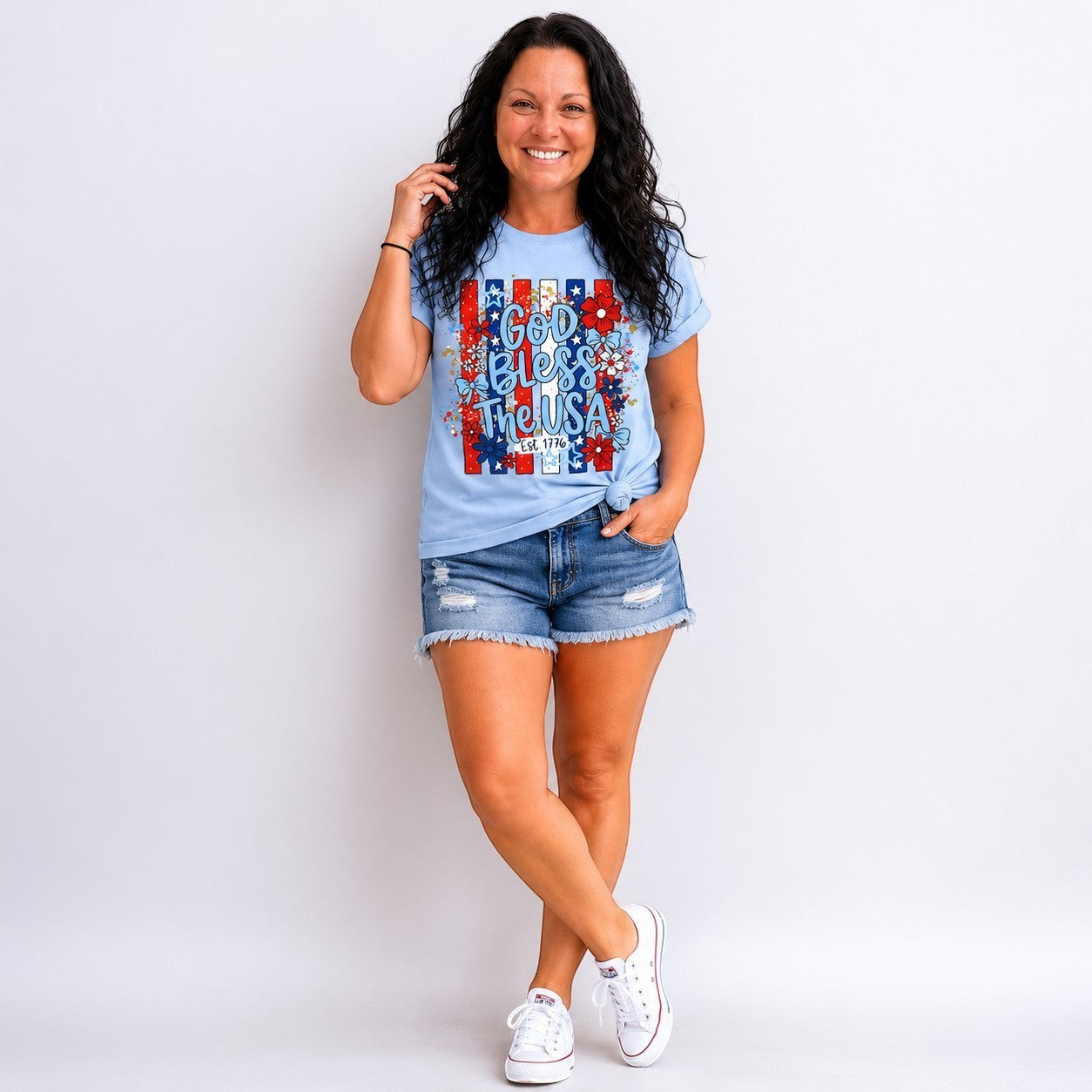 Tea-Shirt Shoppe light blue graphic tee with "God Bless the USA" text, floral accents, and red, white, and blue stripes.