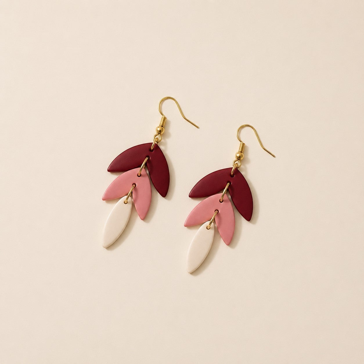 Tea-Shirt Shoppe handcrafted clay earrings with three layered leaf shapes in burgundy, dusty rose, and cream.