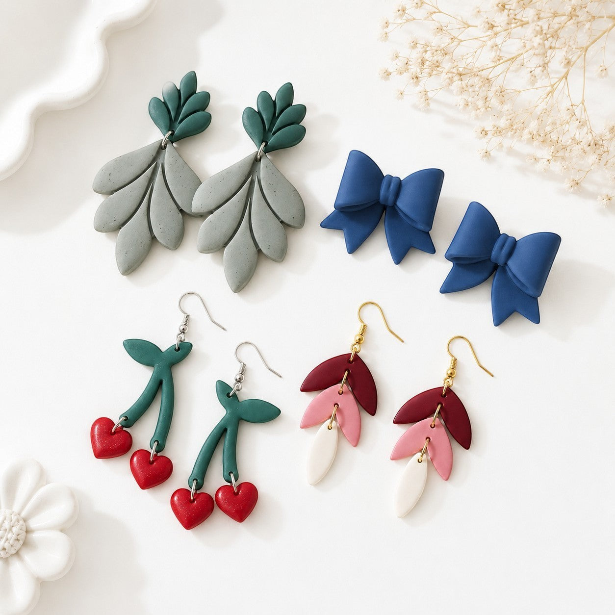 Tea-Shirt Shoppe handcrafted clay earrings: leaf design in grey/green, cherry hearts in red, and blue bows.