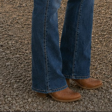 Tea-Shirt Shoppe Judy Blue dark wash bootcut jeans with subtle embossed pattern paired with brown western boots.