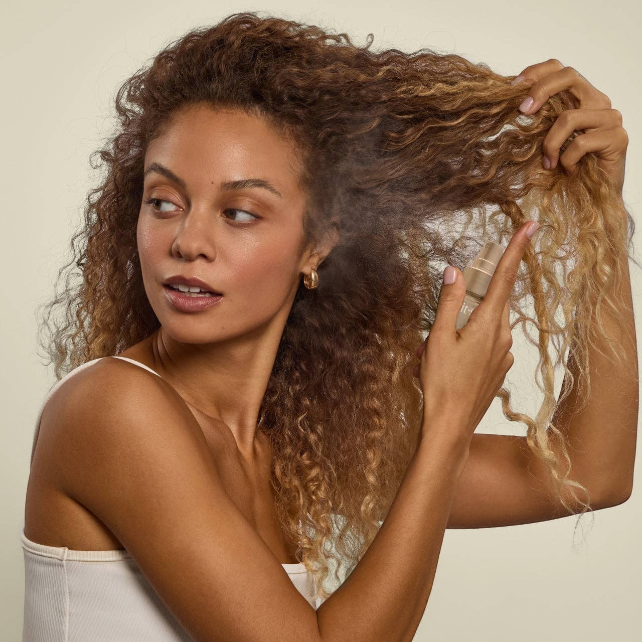 Tea-Shirt Shoppe KITSCH Pistachio Latte hair and body perfume mist being sprayed onto curly hair by a woman.