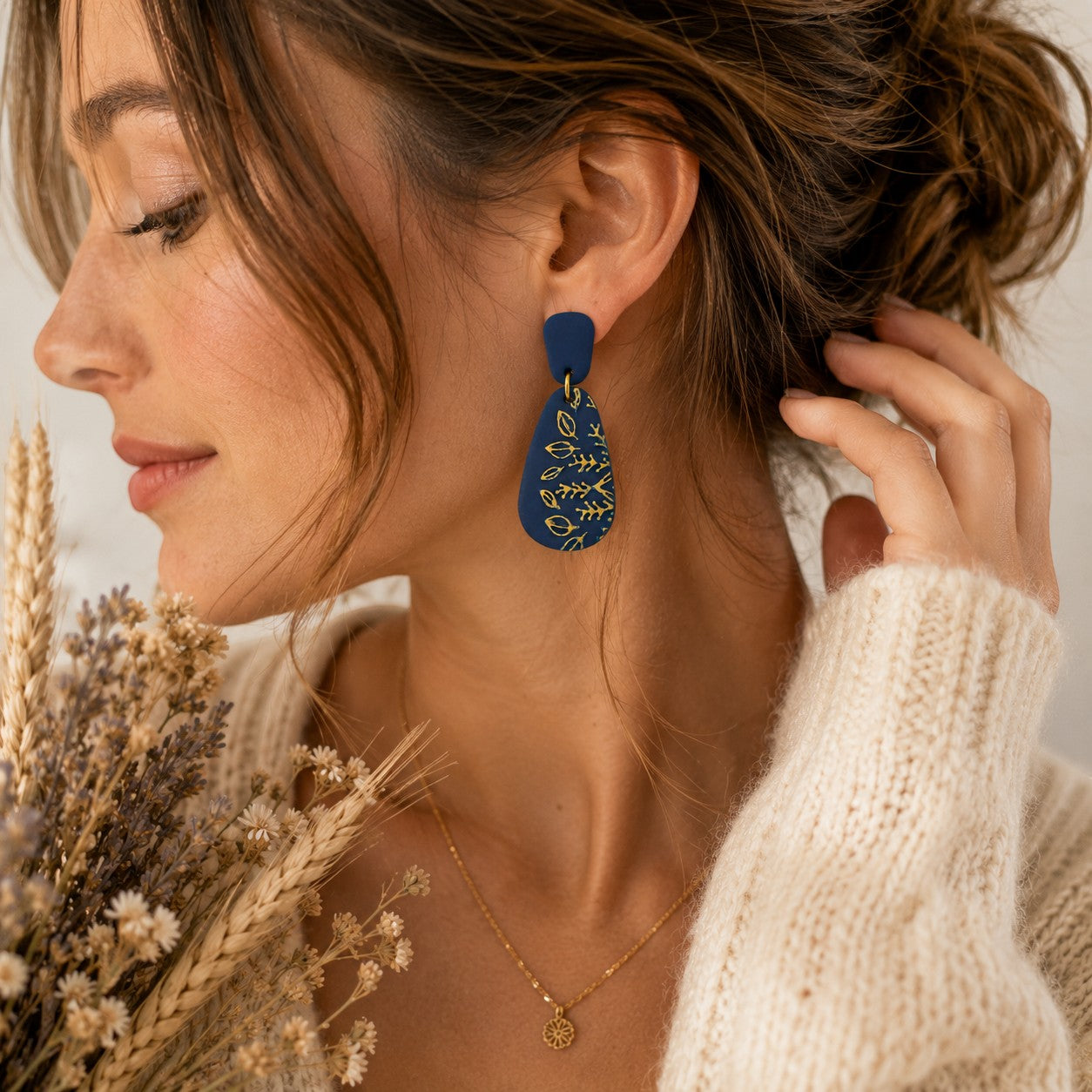 Tea-Shirt Shoppe navy blue polymer clay teardrop earrings with gold botanical details worn by a woman in a sweater.