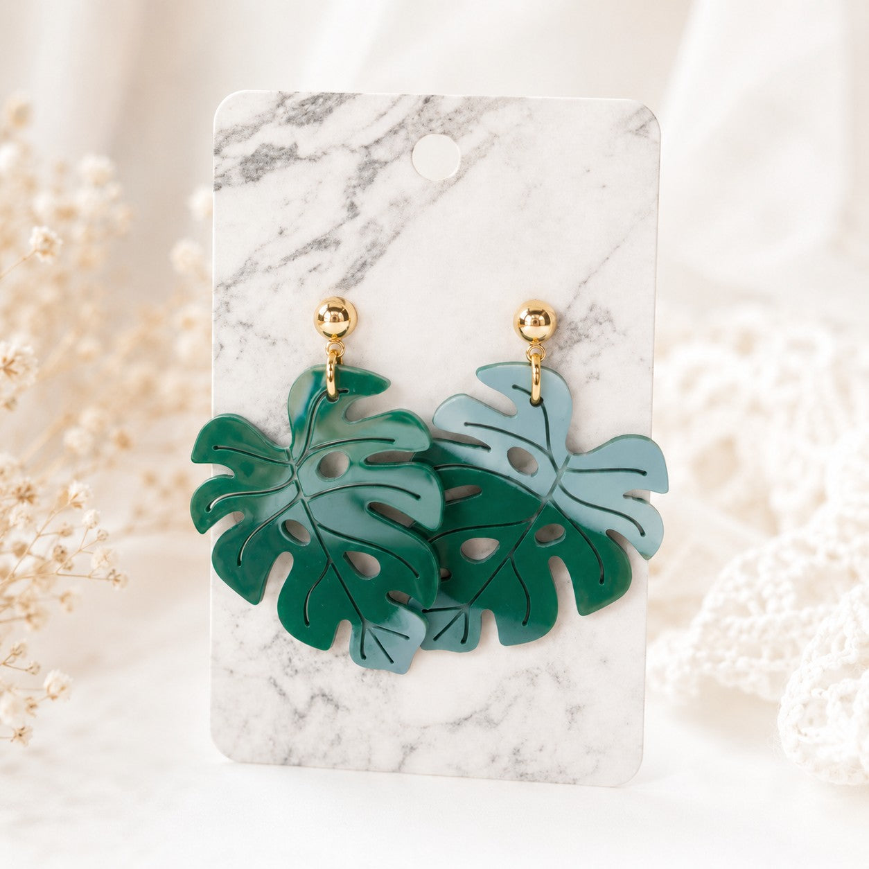 Tea-Shirt Shoppe Palm & Petal Collection monstera leaf earrings in green and teal acrylic with gold studs.