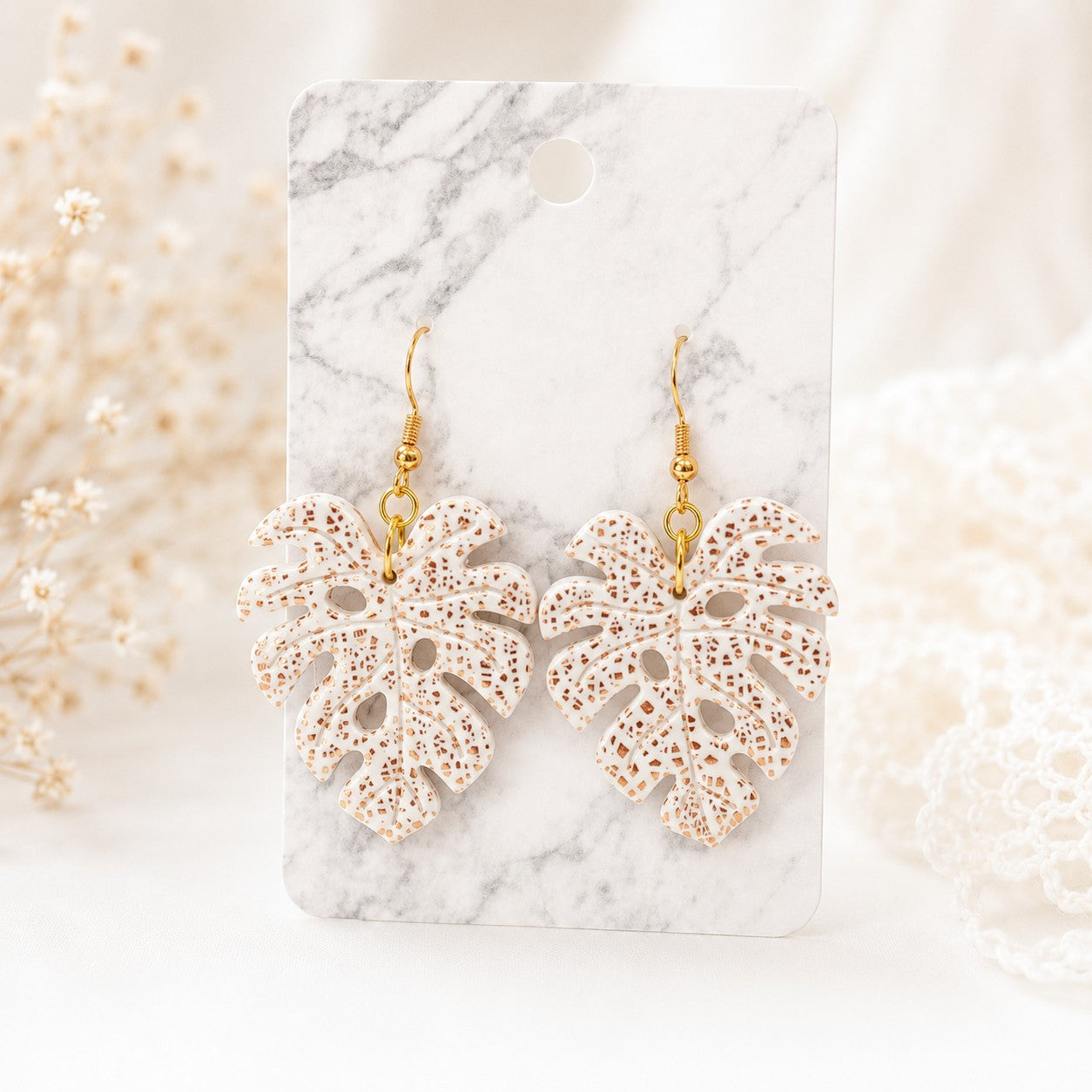 Tea-Shirt Shoppe Palm & Petal Collection monstera leaf earrings in white and gold speckled clay on marble display card
