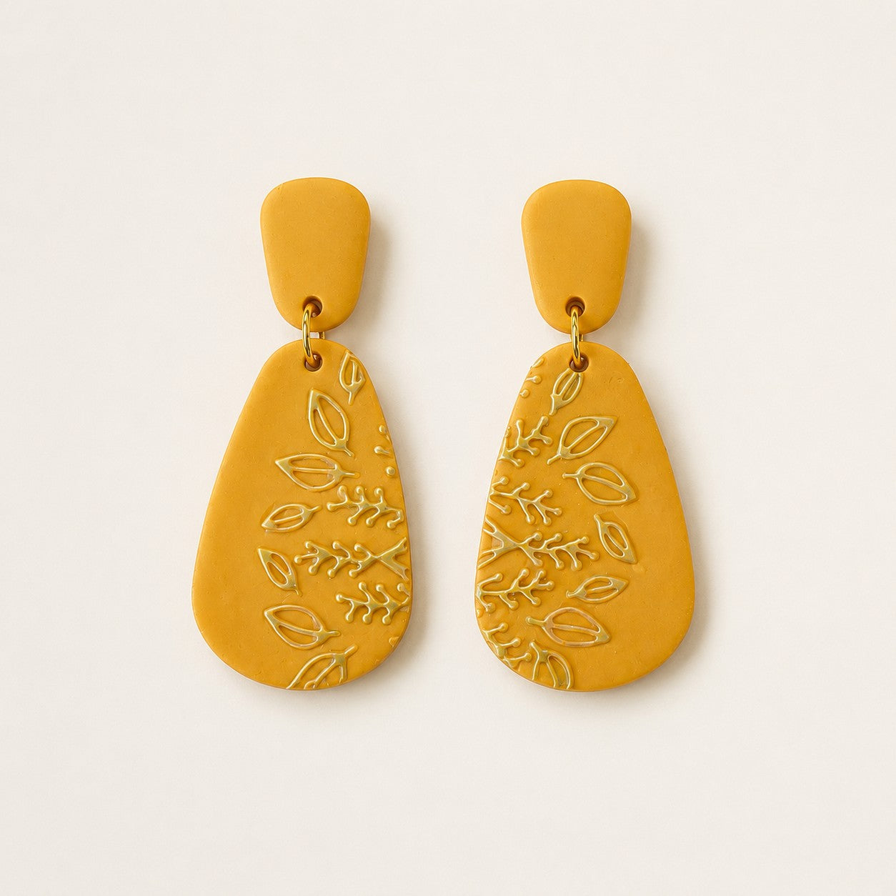 Tea-Shirt Shoppe mustard yellow teardrop dangle earrings with embossed botanical leaf patterns and surgical steel posts.