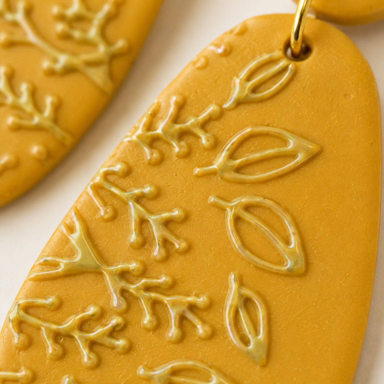 Tea-Shirt Shoppe mustard yellow teardrop dangle earrings with embossed botanical leaf and wildflower patterns.