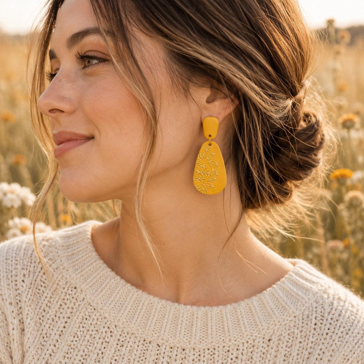 Tea-Shirt Shoppe mustard yellow teardrop dangle earrings with embossed botanical leaf pattern worn by a woman.