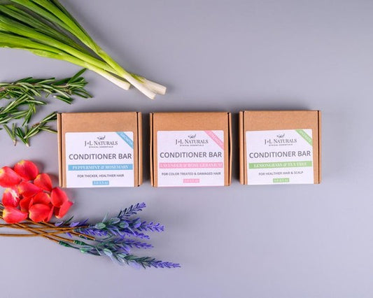 Tea-Shirt Shoppe J&L Naturals vegan conditioner bars in three scents with botanical ingredients on a grey background.