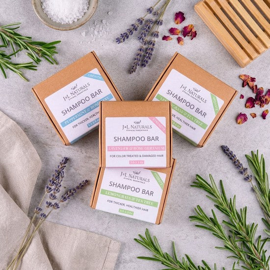 Tea-Shirt Shoppe natural shampoo bars in eco-friendly boxes with lavender, rosemary, and rose petals on stone surface
