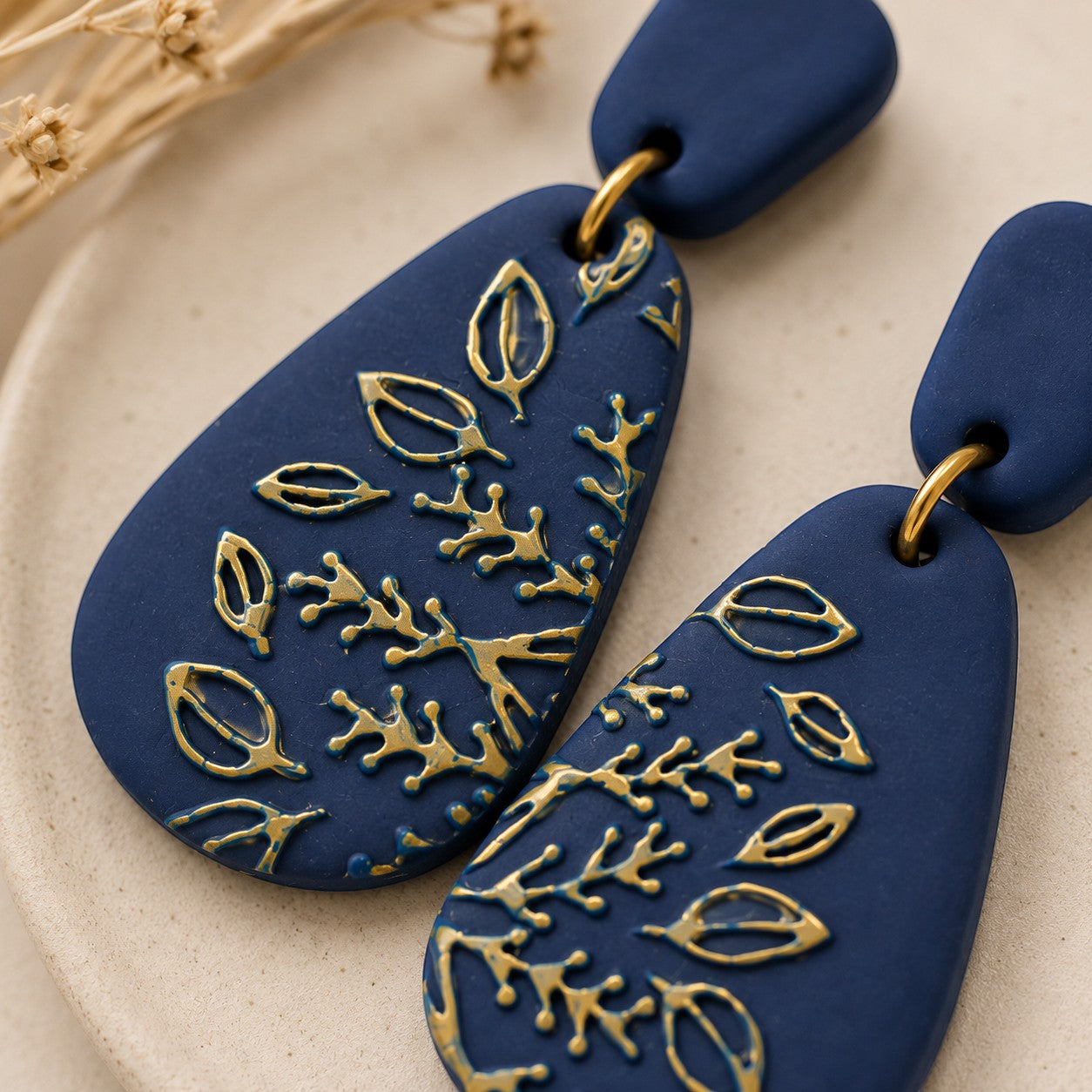 Tea-Shirt Shoppe Midnight Meadow teardrop dangle earrings in matte navy blue polymer clay with gold botanical details.