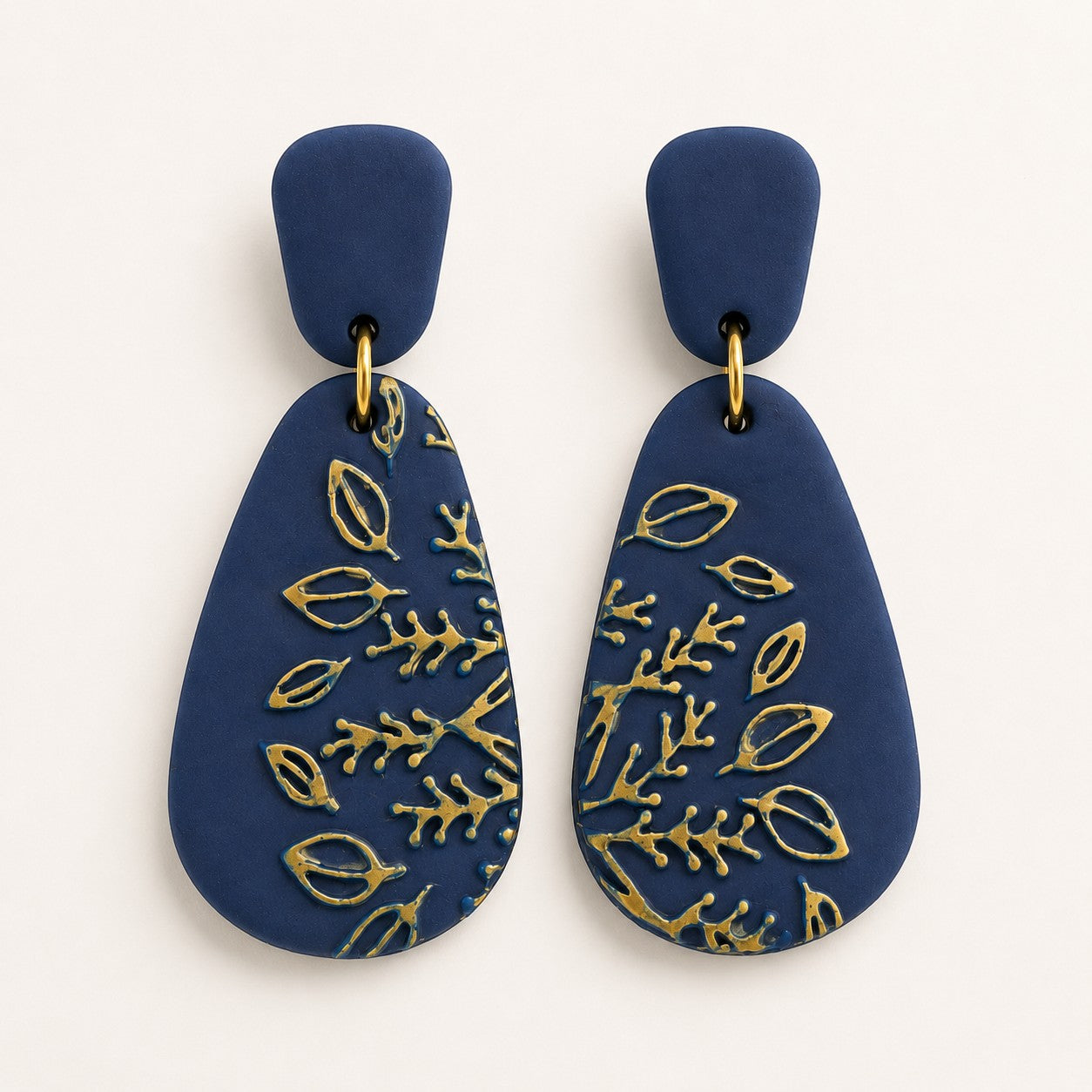 Tea-Shirt Shoppe navy blue polymer clay teardrop dangle earrings with embossed gold botanical leaf patterns.
