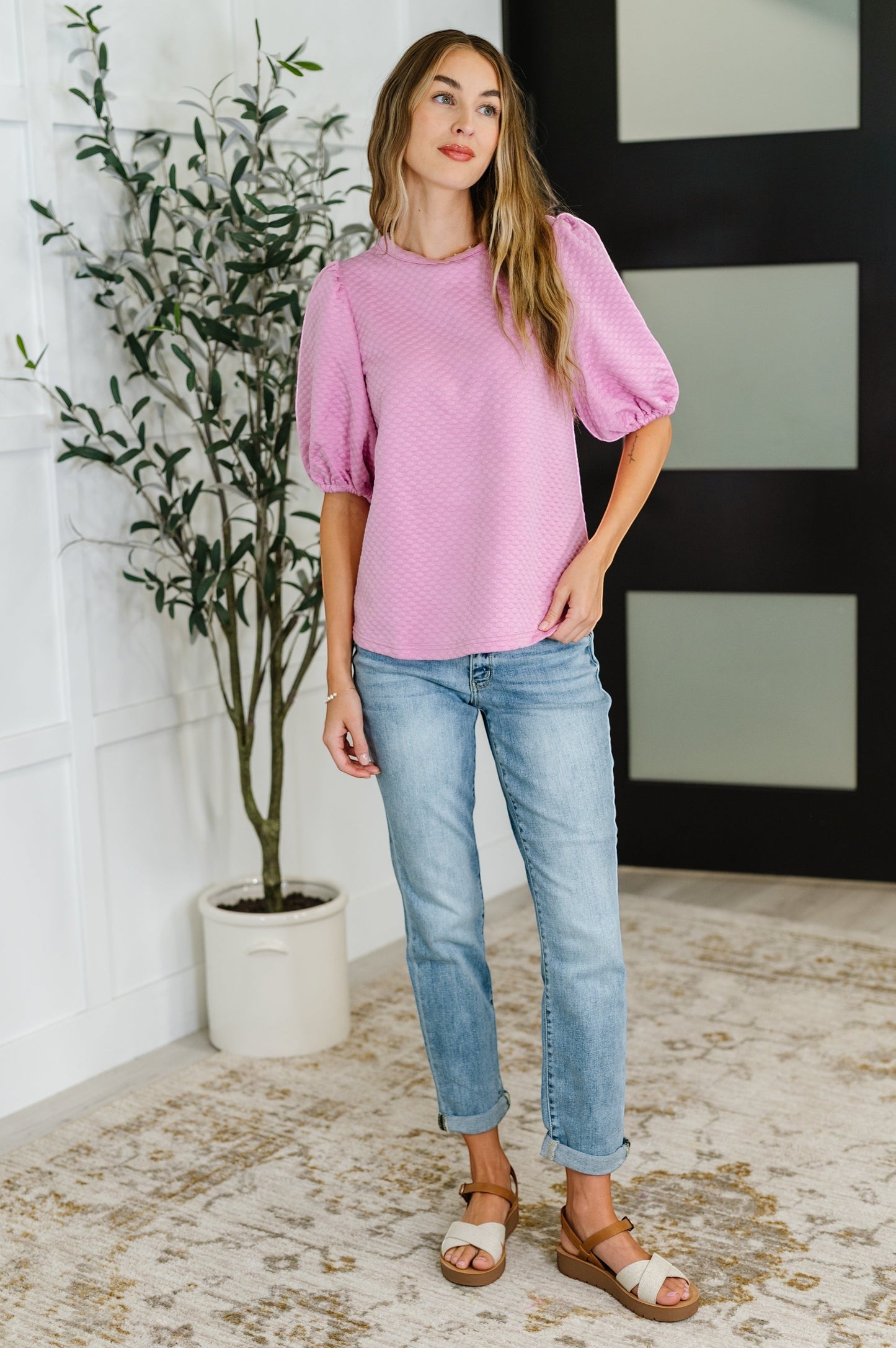 Tea-Shirt Shoppe pink textured balloon sleeve blouse with round neckline worn by a model with light wash jeans.