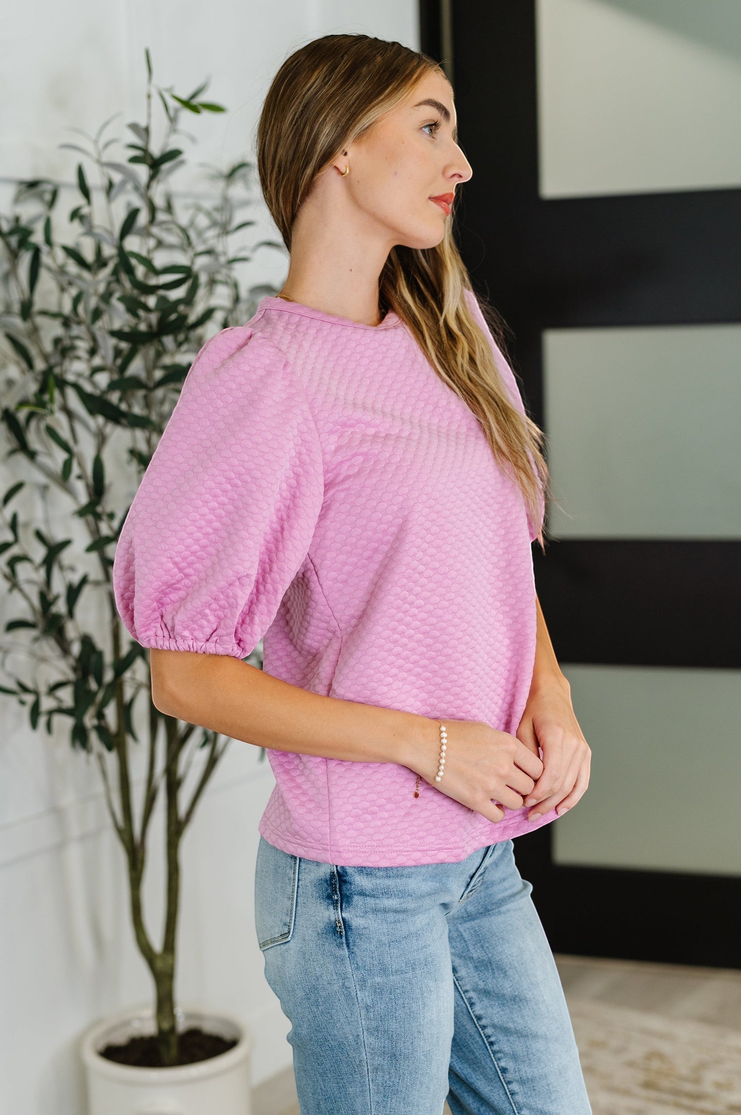 Tea-Shirt Shoppe pink textured knit blouse with puff sleeves and round neckline worn by a model in profile view.