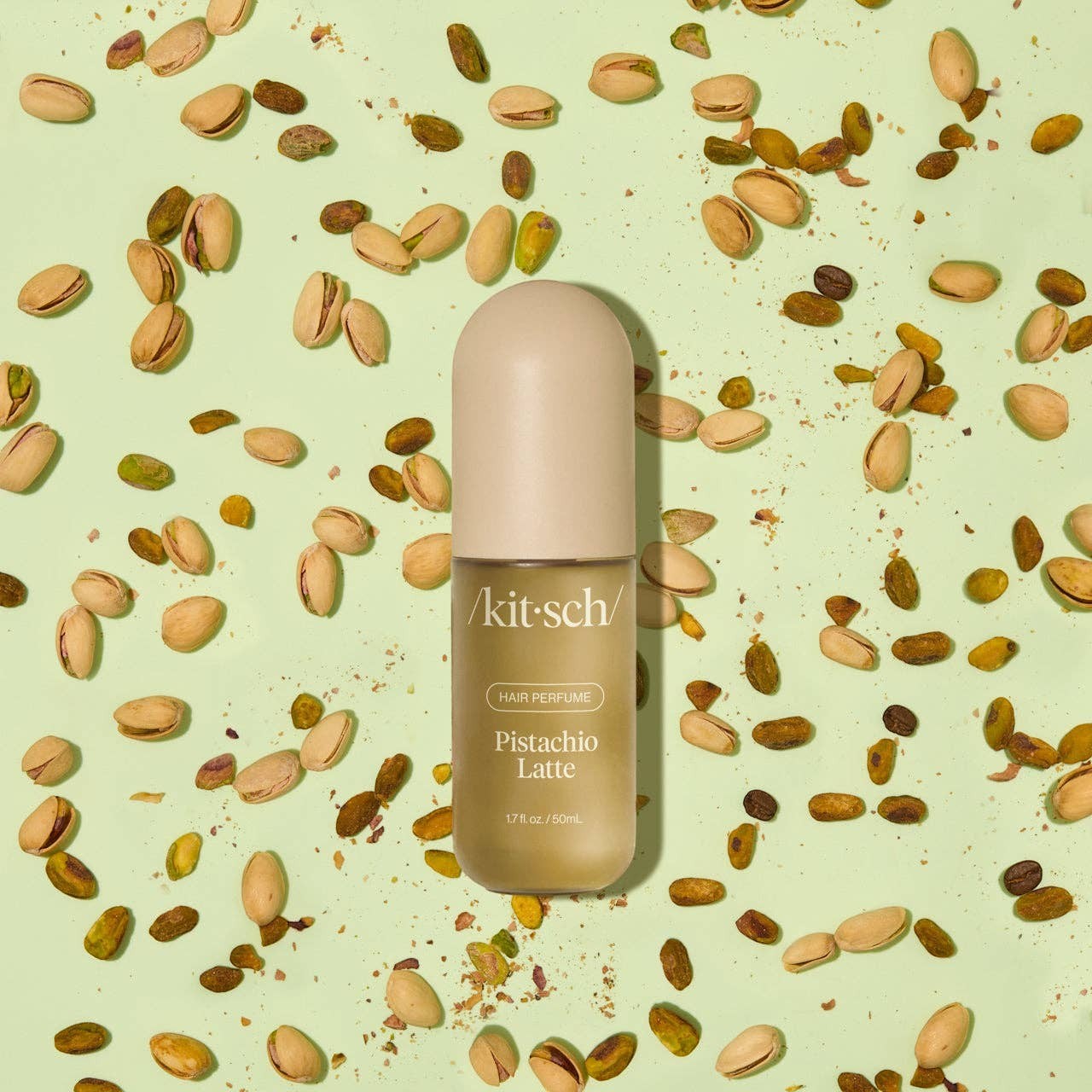 Tea-Shirt Shoppe KITSCH Pistachio Latte hair and body perfume mist bottle surrounded by scattered pistachio nuts.
