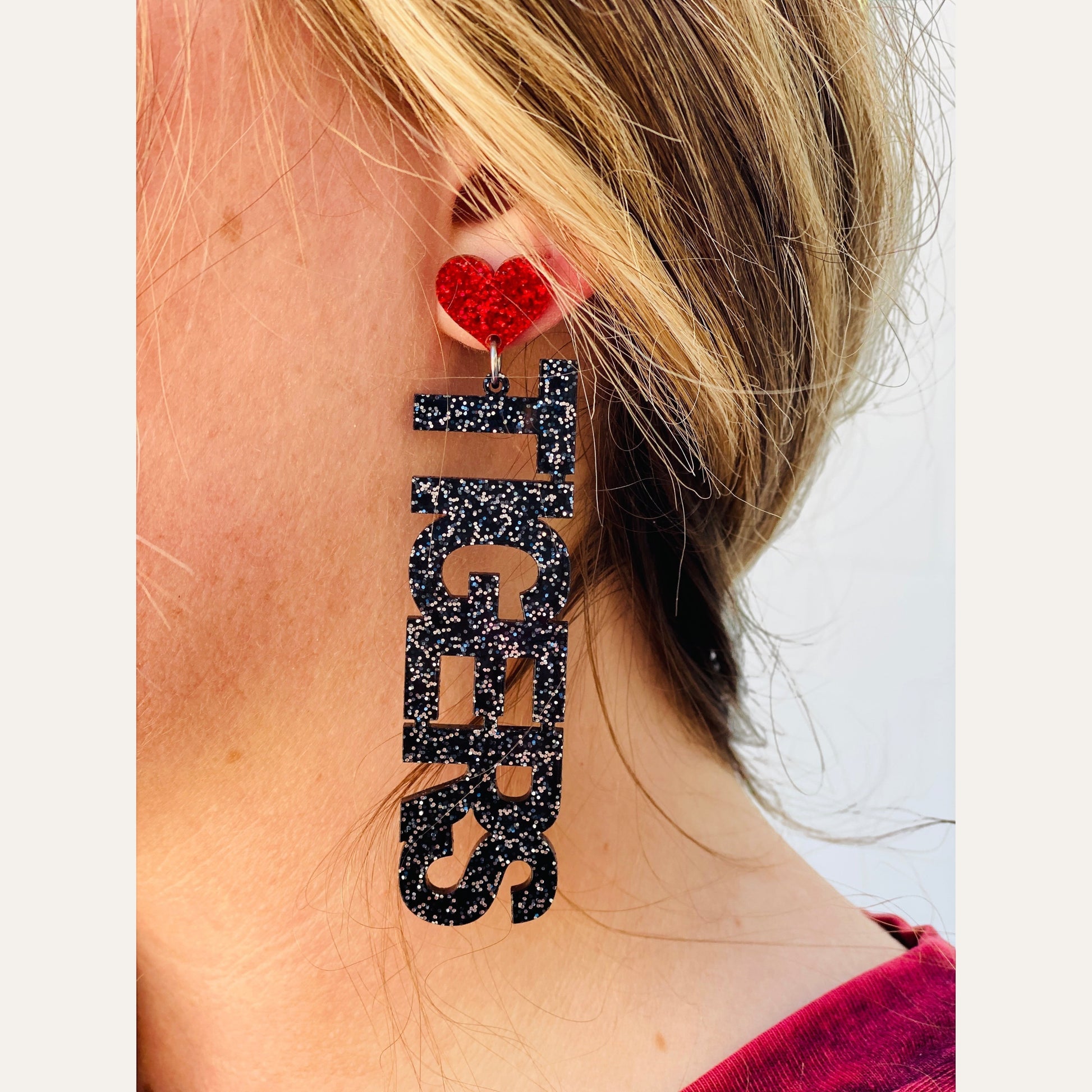 Tea-Shirt Shoppe black glitter TIGERS drop earrings with a red heart accent worn by a woman.