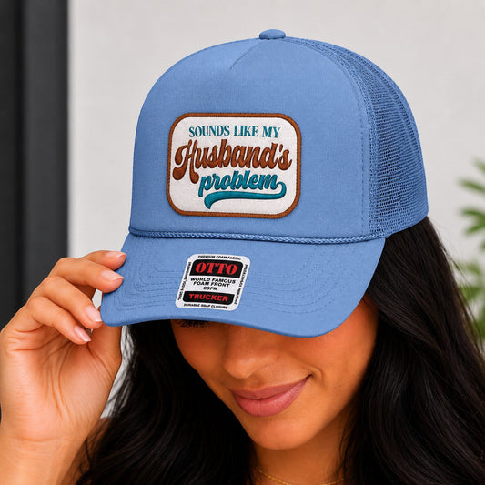 Tea Shirt Shoppe Wholesale light blue trucker hat with "Sounds Like My Husband's Problem" embroidered patch.